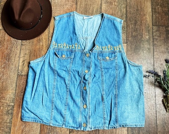 May include: A light blue denim vest with a button front closure and two pockets. The vest has a gold embroidered design around the neckline.