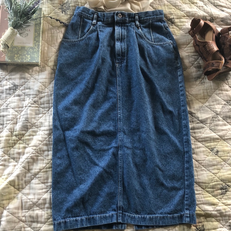May include: A blue denim skirt with a high waist and a straight cut. The skirt has a button and zipper closure and two pockets on the front.