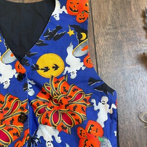 May include: A blue Halloween vest with a black back and buttons. The vest features a festive print of orange jack-o'-lanterns, white ghosts, bats, and a large orange bow. The vest is a fun and unique addition to any Halloween costume.
