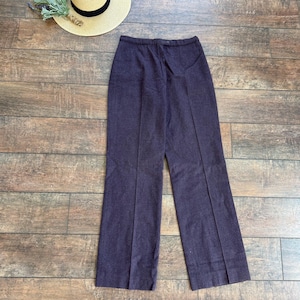 May include: A pair of dark purple, high-waisted trousers with a button closure and a straight leg. A straw hat with a black band and a bundle of dried lavender are also present.