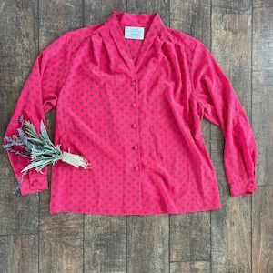 May include: A pink long-sleeved button-up shirt with a black geometric pattern. The shirt has a collar and a button-up front.