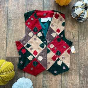 May include: A patchwork vest with a quilted design featuring green, red, brown, and beige squares with embroidered leaves. The vest has a button closure and a label that reads "Country Classics".