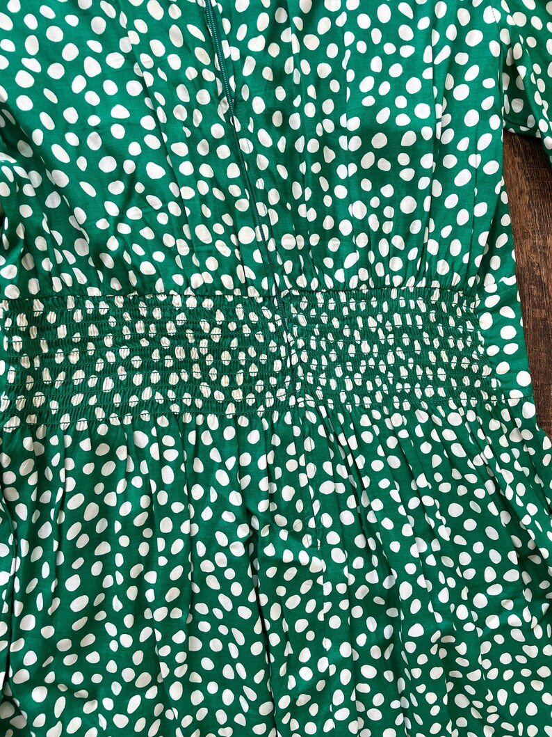 May include: Green dress with a white polka dot pattern. The dress has a fitted bodice and a gathered skirt. The dress has a zipper closure in the back.