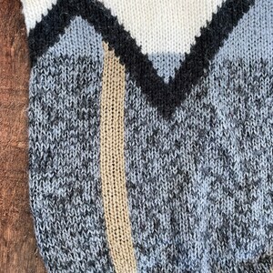 May include: A close-up of a knitted sweater with a geometric pattern in shades of white, black, gray, and beige.