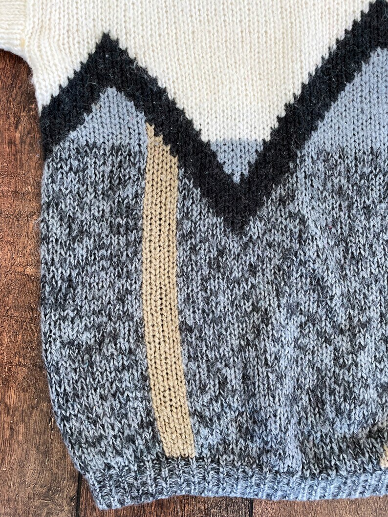 May include: A close-up of a knitted sweater with a geometric pattern in shades of white, black, gray, and beige.
