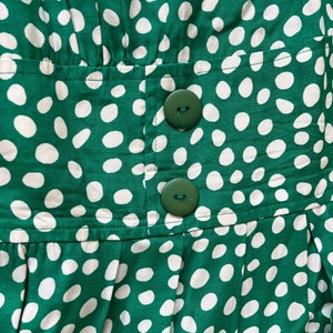 May include: Green fabric with white polka dots and two green buttons. The fabric is pleated and has a seam running horizontally across the middle.