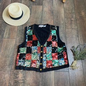May include: A black sequined vest with a checkered pattern in shades of red, green, blue, and silver. The vest has a V-neck and button closure.