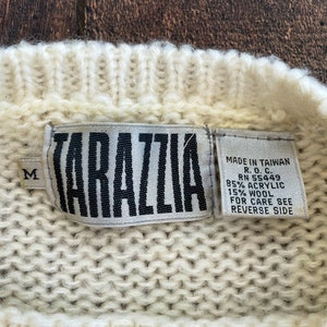 May include: White knitted sweater with a white tag that says "KARAZZIA" and "MADE IN TAIWAN R.O.C. RN 55449 85% ACRYLIC 15% WOOL FOR CARE SEE REVERSE SIDE".