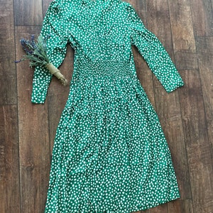 May include: A green midi dress with a white polka dot pattern. The dress has long sleeves and a v-neckline.
