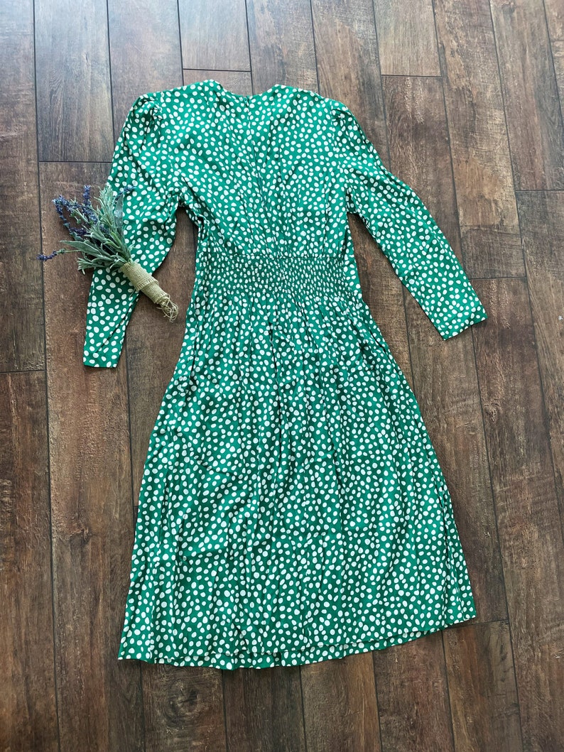 May include: A green midi dress with a white polka dot pattern. The dress has long sleeves and a v-neckline.