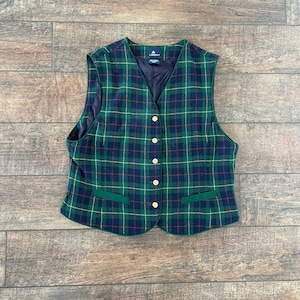 May include: A green, blue, red, and gold plaid vest with a green trim and gold buttons. The vest has two pockets.