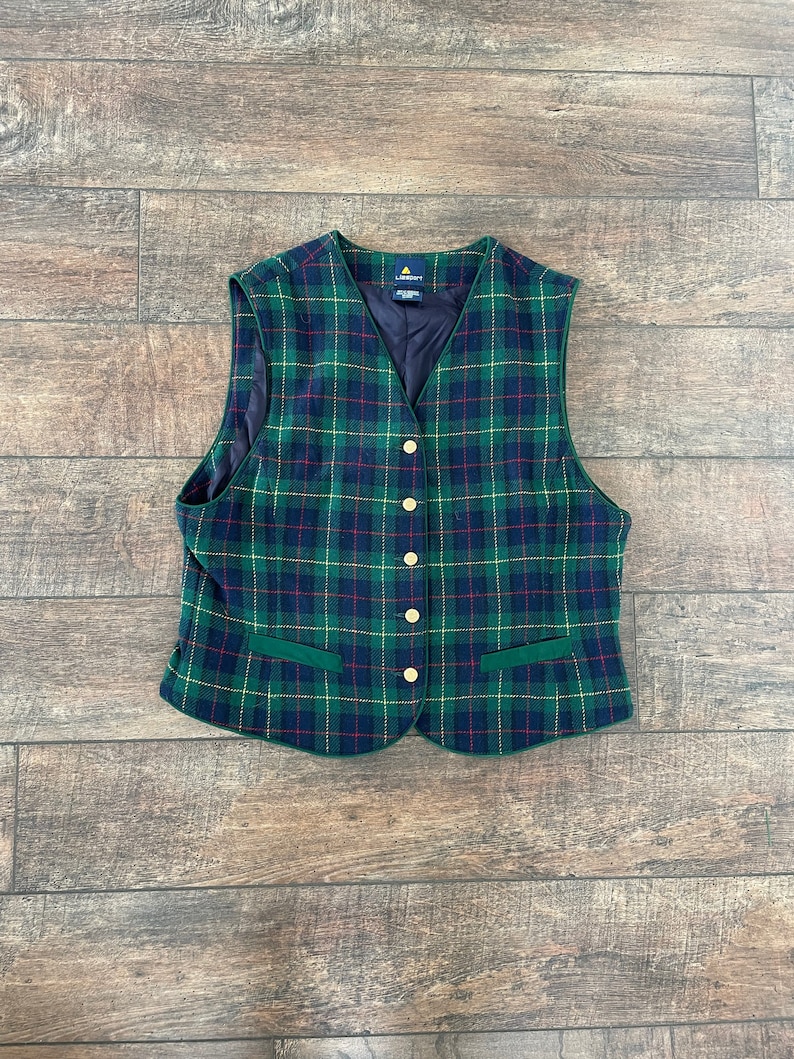 May include: A green, blue, red, and gold plaid vest with a green trim and gold buttons. The vest has two pockets.
