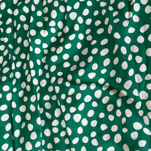 May include: Green fabric with a white polka dot pattern. The fabric is wrinkled and has a soft texture.