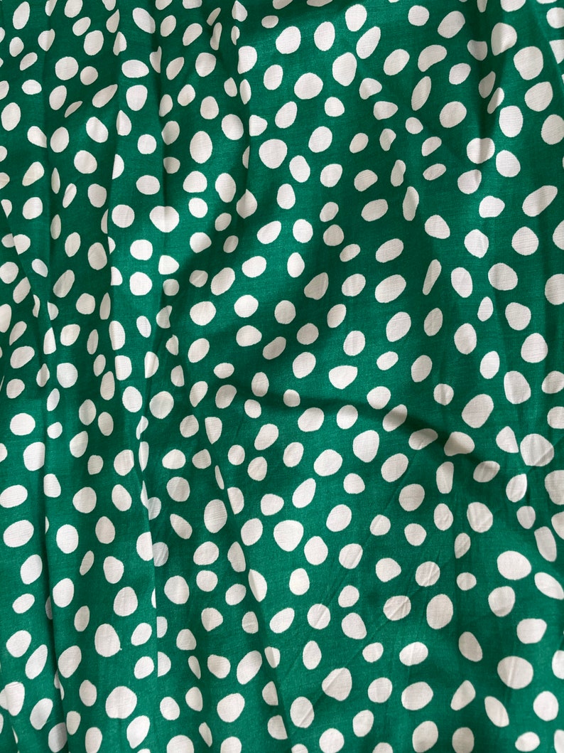 May include: Green fabric with a white polka dot pattern. The fabric is wrinkled and has a soft texture.