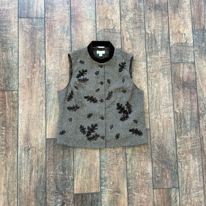 May include: A brown tweed waistcoat with a velvet collar and a button fastening. The waistcoat is decorated with brown embroidered leaves.