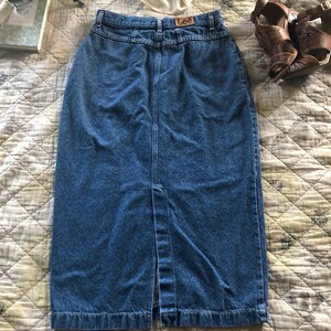 May include: A blue denim skirt with a front slit and a button closure. The skirt has a brown leather label with the word "Lee" on it.