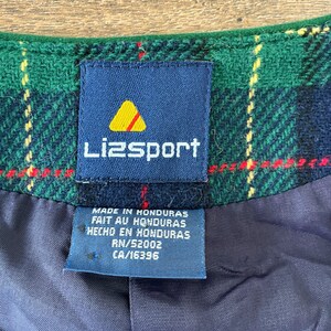 May include: A blue and white Lizsport label with a yellow triangle logo. The label is attached to a green and black plaid fabric. The label reads "Made in Honduras, Fait au Honduras, Hecho en Honduras, RN/52002, CA/16396".