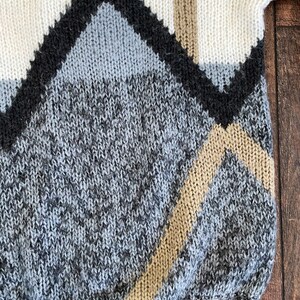 May include: A knitted sweater with a geometric pattern in shades of white, gray, black, and beige.
