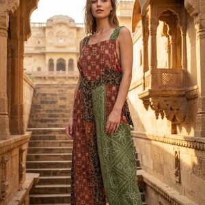 Op de afbeelding: Een mouwloze jumpsuit met een patchworkontwerp in een mix van roestrode, olijfgroene en donkerbruine stoffen met patronen. Het kledingstuk heeft een vierkante halslijn, een wijde, kortere broek en een getailleerd lijfje.