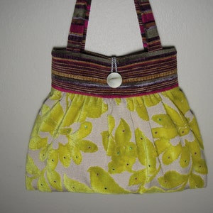 Puede incluir: Un bolso de mano de tela amarillo y beige con un estampado floral. El bolso tiene un ribete de tela a rayas marrón y rosa y un botón blanco.
