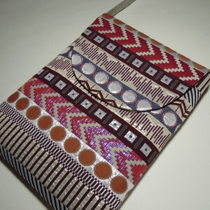 May include: A small, patterned crossbody bag with a flap closure. The bag is made of a fabric with a geometric design in shades of red, white, and gray. The strap is a light brown color.