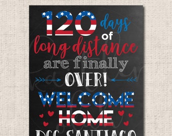 May include: A black chalkboard sign with red, white, and blue stars and stripes design. The sign reads "120 days of long distance are finally over! Welcome Home DCC Santiago".