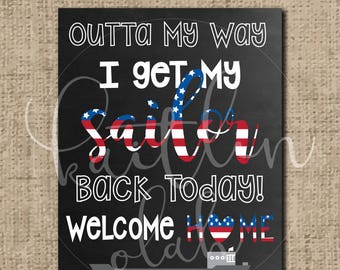 May include: A black chalkboard sign with white text that reads "Outta my way I get my sailor back today! Welcome home" with a red, white, and blue American flag design. The sign also includes a small ship graphic and the text "DCC Solange".