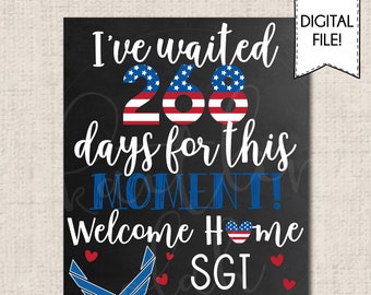 May include: A black chalkboard sign with the text "I've waited 268 days for this moment! Welcome home SGT Bronner". The numbers 268 are decorated with an American flag design. The sign also features a blue Air Force logo and a red heart with an American flag design.