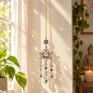 May include: A hanging suncatcher featuring a gold-toned metal lotus flower charm, light blue beads, and three clear faceted crystal prisms suspended from a gold chain. The design includes small sun-shaped metal accents and a circular charm.