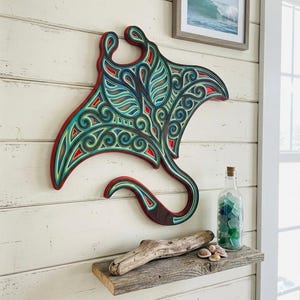 May include: A multi-layered wooden wall art piece shaped like a manta ray, featuring intricate cutouts and a vibrant color palette of teal, blue, red, and natural wood tones. The design displays swirling patterns and geometric shapes throughout.
