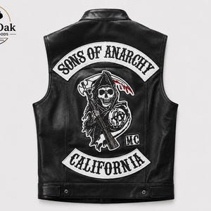 Könnte beinhalten: Eine schwarze Lederweste mit einem großen Rückenaufnäher, der den Text SONS OF ANARCHY und CALIFORNIA in Weiß zeigt. Die zentrale Grafik stellt einen Sensenmann mit einem Gewehr und einer Weltkugel mit Anarchie-Symbol dar, ergänzt durch MC.