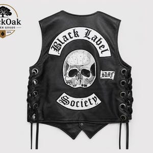 Könnte beinhalten: Eine schwarze Lederweste mit seitlicher Schnürung durch schwarze Kordeln und Metallösen. Auf der Rückseite befindet sich ein großer weißer Aufnäher mit dem Text Black Label Society in gotischer Schrift, ein Totenkopfmotiv und ein kleinerer Aufnäher mit SDMF.