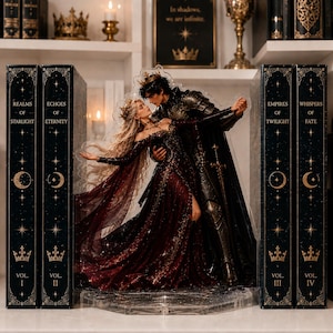 Puede incluir: Un soporte de acrílico transparente que muestra a una pareja con ropa formal bailando, colocado entre cuatro libros azul oscuro titulados Realms of Starlight, Echoes of Eternity, Empires of Twilight y Whispers of Fate.