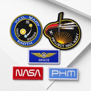 May include: Five embroidered patches featuring space-themed designs. One circular blue patch reads HAIL MARY EARTH, one black shield-shaped patch reads PROJECT HAIL MARY, one blue rectangular patch reads GRACE, one red rectangular patch reads NASA, and one light blue rectangular patch reads PHM.