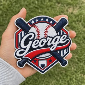 Puede incluir: Un parche bordado circular que presenta una pelota de béisbol blanca con costuras rojas, bates de béisbol azul oscuro cruzados y el nombre George en letra cursiva blanca. El diseño incluye un fondo de escudo rojo y azul con estrellas blancas.