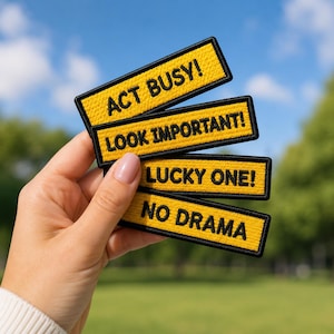 May include: Four rectangular embroidered patches with yellow backgrounds and black borders. The patches feature black text that reads: ACT BUSY!, LOOK IMPORTANT!, LUCKY ONE!, and NO DRAMA. Each patch has a textured fabric surface.