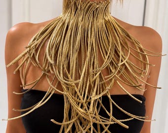 May include: A gold-colored statement necklace featuring a high collar design composed of numerous thin, flexible, metallic-looking strands that drape downward over the chest, creating a fringe-like effect that covers the upper torso area.
