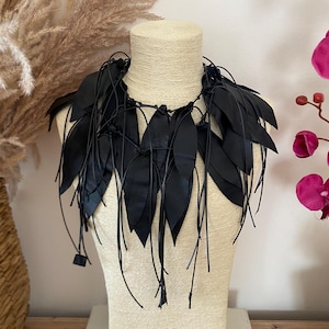 Puede incluir: Un collar negro llamativo que presenta m&uacute;ltiples recortes en forma de hoja unidos a una serie de cordones negros finos. El dise&ntilde;o consiste en elementos negros puntiagudos y superpuestos que caen alrededor del cuello, creando una apariencia texturizada con flecos.
