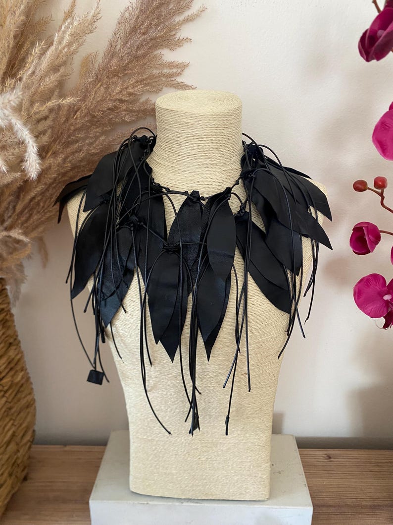 Puede incluir: Un collar negro llamativo que presenta m&uacute;ltiples recortes en forma de hoja unidos a una serie de cordones negros finos. El dise&ntilde;o consiste en elementos negros puntiagudos y superpuestos que caen alrededor del cuello, creando una apariencia texturizada con flecos.