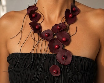 May include: A necklace featuring multiple dark burgundy, petal-shaped elements arranged along thin black cords. Each petal-shaped piece is accented with a small, round, matching burgundy bead at its center, creating a cascading, organic design.