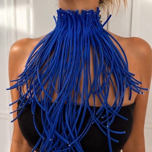 Puede incluir: Un collar tipo gargantilla de color azul vibrante construido con numerosos hilos delgados, flexibles y similares a cordones que caen desde el cuello, creando un efecto de flecos denso y superpuesto que cubre la parte superior del pecho.