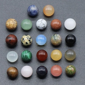 Può includere: Una collezione di venti perline sferiche e lisce disposte in una griglia. Le perline presentano vari colori e motivi, tra cui bianco, nero, blu, verde, giallo, arancione, rosa, marrone a tinta unita e disegni maculati o marmorizzati.