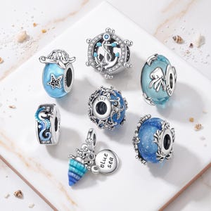 May include: A collection of seven silver charm beads with nautical themes, including a ship wheel with an anchor, a sea turtle, a seahorse, a jellyfish, and a shell charm with a tag reading blue sea, all featuring blue enamel and clear stones.