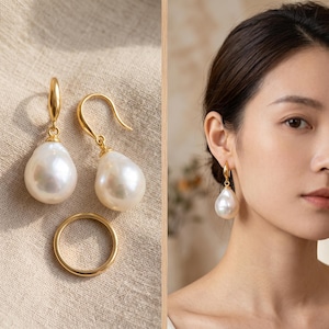 May include: A pair of gold drop earrings featuring large, teardrop-shaped white pearls suspended from curved gold hooks, accompanied by a simple, smooth gold band ring. The earrings are shown worn on an earlobe, highlighting the pearl luster.