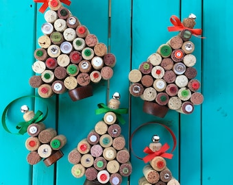 May include: Handmade Christmas tree ornaments crafted from wine corks and colorful buttons. Each tree features a small bell and ribbon for hanging. The trees are arranged on a turquoise wooden surface.