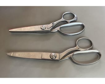 May include: Two pairs of silver-toned metal scissors with large finger loops. The bottom pair features the engraved text WISS NEWARK N.J. U.S.A. on the blade. Both tools have a central pivot screw and polished metallic finish throughout the handles.