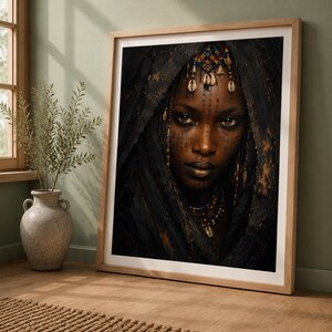 May include: A framed portrait print featuring a close-up of a person with dark skin, wearing a dark textured head covering, intricate beaded jewellery, and cowrie shell accents. The person has facial markings and a direct gaze, presented in a light wood frame.