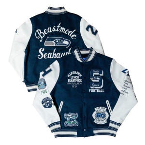 May include: A navy blue and white varsity jacket featuring embroidered Seattle Seahawks logos and text including Beastmode, Marshawn Lynch, and various championship years. The jacket has white sleeves, a snap-button front, and striped ribbed trim.