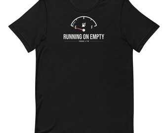 May include: A black short-sleeve t-shirt featuring a white graphic of a fuel gauge with the needle pointing to E. Below the gauge, the text reads RUNNING ON EMPTY in white, followed by the smaller text TORQUE & TIN in a thin white font.