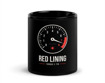 May include: A black ceramic mug featuring a white tachometer graphic with a red zone starting at 7,000 RPM. Below the gauge, the text reads RED LINING in white, followed by the smaller text TORQUE & TIN with a red horizontal line.